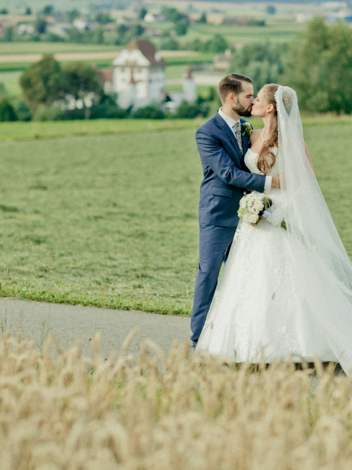 küssendes Brautpaar auf dem Feld im Hintergrund das Wasserschloss Wyher